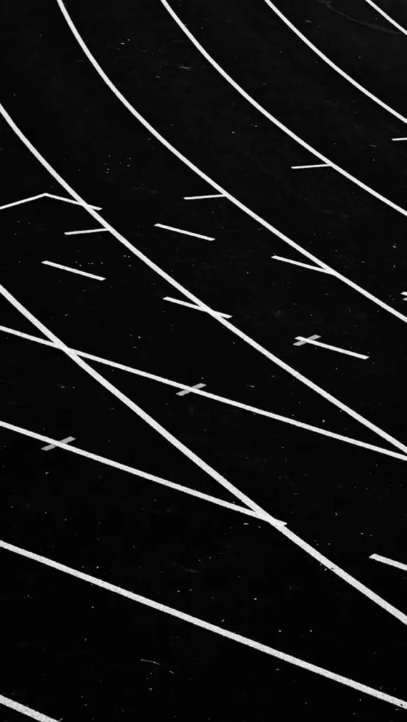 Imagem em preto e branco representando linhas curvas sobre uma superfície escura, evocando uma pista de atletismo. Essas linhas formam um padrão abstrato e dinâmico que sugere movimento.
