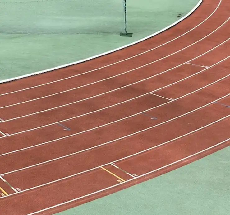 Uma seção curva de uma pista de atletismo vazia, com corredores de um vermelho vibrante e linhas brancas, destacando-se sobre um fundo verde contrastante, que transmite uma atmosfera serena e bem organizada.